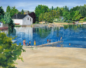 Beach beside deep blue lake with white boat house and green trees